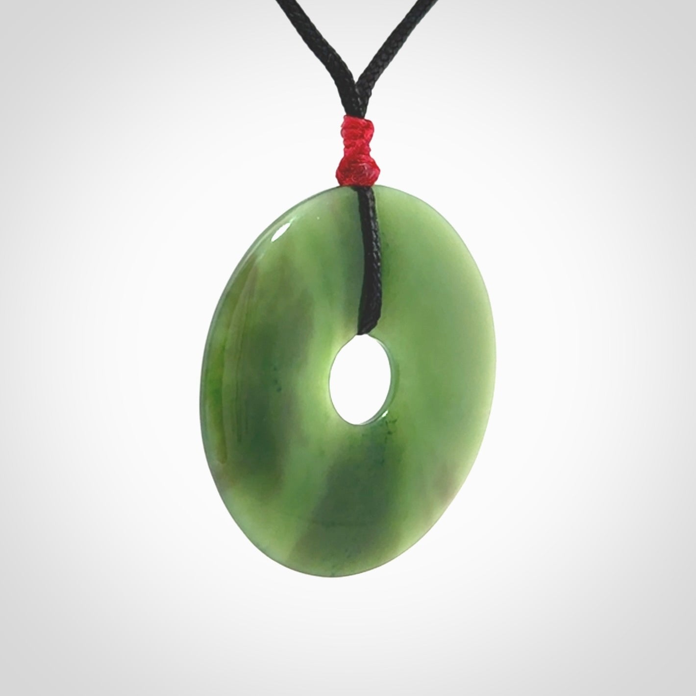 This picture shows a large hand-carved disc pendant. It is carved from British Columbian jade and is suspended from a hand-plaited, black cord. Free delivery worldwide. BC Jade contemporary necklace.