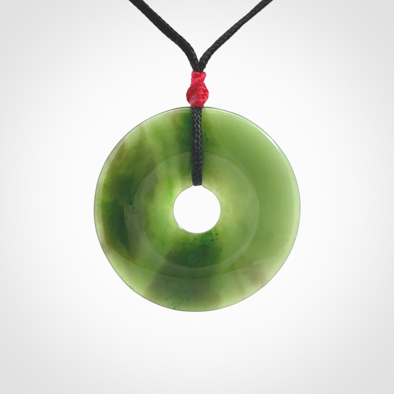 This picture shows a large hand-carved disc pendant. It is carved from British Columbian jade and is suspended from a hand-plaited, black cord. Free delivery worldwide. BC Jade contemporary necklace.
