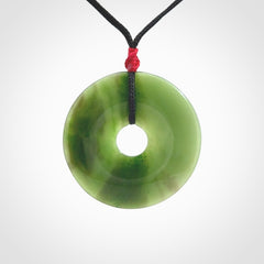 This picture shows a large hand-carved disc pendant. It is carved from British Columbian jade and is suspended from a hand-plaited, black cord. Free delivery worldwide. BC Jade contemporary necklace.