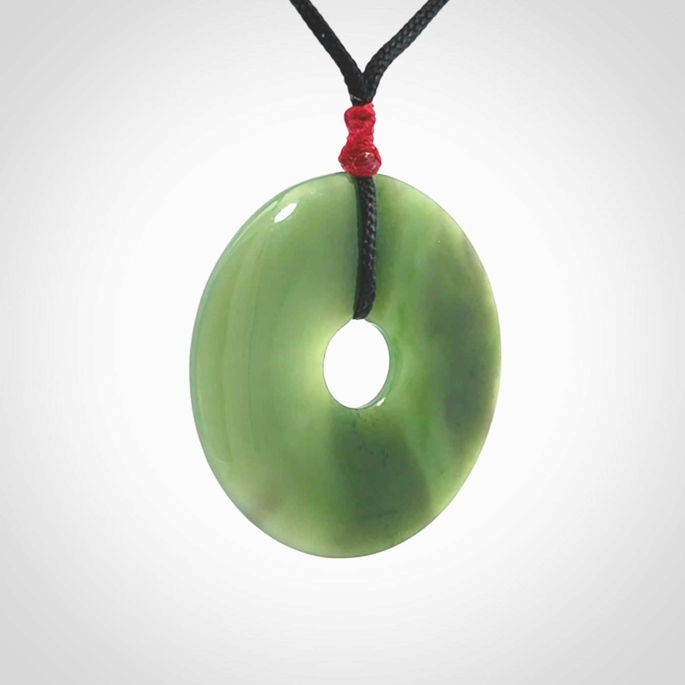 This picture shows a large hand-carved disc pendant. It is carved from British Columbian jade and is suspended from a hand-plaited, black cord. Free delivery worldwide. BC Jade contemporary necklace.