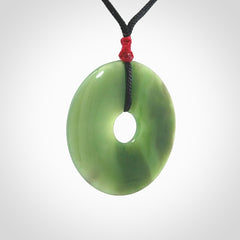 This picture shows a large hand-carved disc pendant. It is carved from British Columbian jade and is suspended from a hand-plaited, black cord. Free delivery worldwide. BC Jade contemporary necklace.