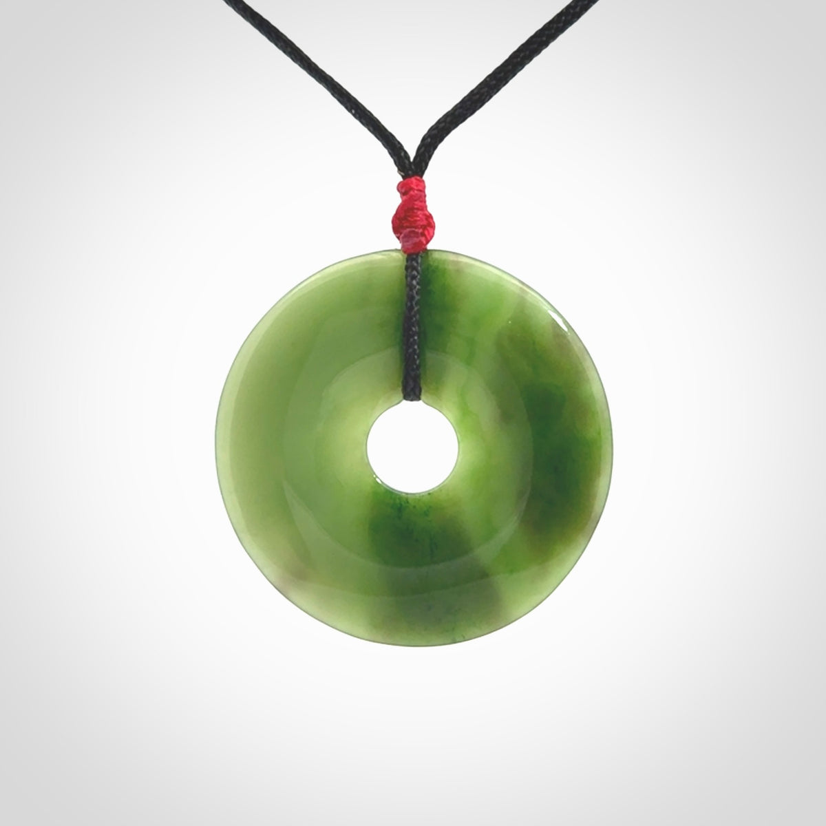 This picture shows a large hand-carved disc pendant. It is carved from British Columbian jade and is suspended from a hand-plaited, black cord. Free delivery worldwide. BC Jade contemporary necklace.