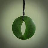 This photo shows a medium sized unique complex contemporary disc pendant. It is carved from a very light and semi translucent speckled piece of New Zealand kawakawa jade. It is finished in a soft matte that glows and is lovely to hold. We provide this with an adjustable cord in plain black. We ship this piece worldwide and shipping is included in the price.