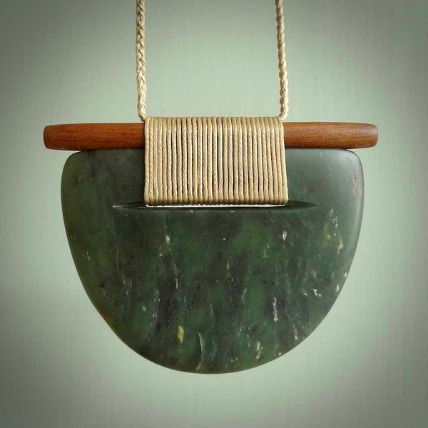 Raukaraka Pounamu breastplate pendant with rata wood. Hand carved by Rhys Hall for NZ Pacific. Handmade jewellery for sale online. The cord is a 3-braid plait in beige and has a loop and pebble toggle closure. Breastplate necklace for men and women. Scandinesian breastplate necklace hand made from New Zealand Jade.
