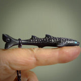 This picture shows a hand carved bone whale shark. It is stained with a special tea dye and is a very detailed piece. It has a hand plaited cord that is length adjustable so that it can be worn as a pendant.