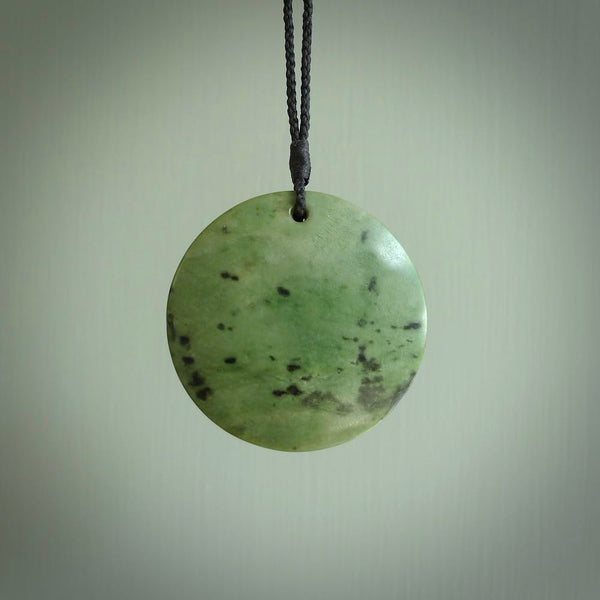 This piece is a large, oval round, disc pendant. It was carved for us by Ric Moor from a lovely deep and milky green piece of New Zealand kokopu jade. It is suspended on a black coloured braided cord that is length adjustable.