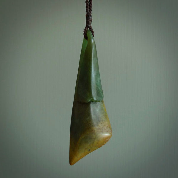 This piece is a large, contemporary, drop pendant. It was carved for us by Ric Moor from a lovely green piece of New Zealand flower jade with orange colours at the base. It is suspended on a beige coloured braided cord that is length adjustable.