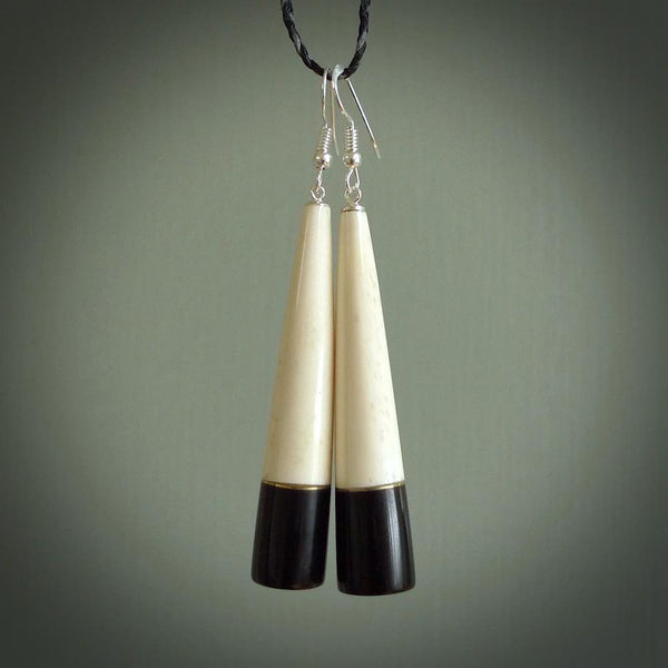 Hand carved earrings made from bone and buffalo horn. They are an elongated drop shape with a flat bottom. The bone is a nice creamy white and incorporates the top three quarters, and the bottom quarter is a beautiful black buffalo horn. These are wonderful handcrafted earrings.