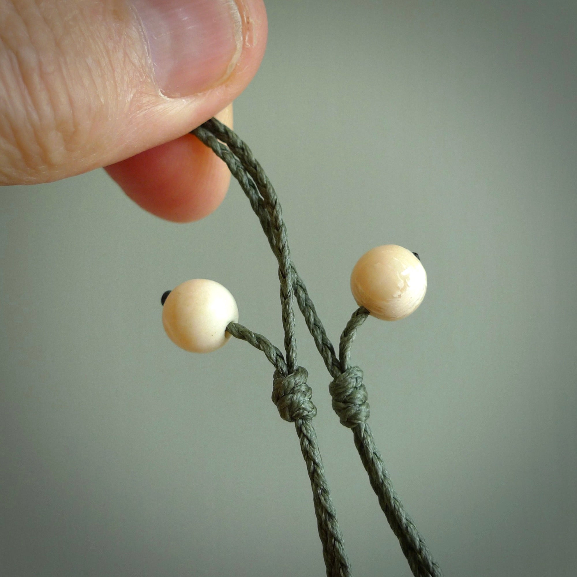 A hand carved and intricate koru pendant made for us by Yuri Terenyi. This is a beautiful little piece and is emblematic of the well known and loved Koru design. It is carved from bone in a round shape with decorative design carved into the koru. It is suspended from a sage cord with a paradise blue floret and the necklace is adjustable.