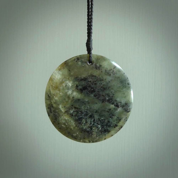This piece is a large sized, oval round, disc pendant. It was carved for us by Raegan Bregman from a lovely green piece of New Zealand Inanga jade and Kokopu Jade. It is suspended on a Black coloured braided cord that is length adjustable.