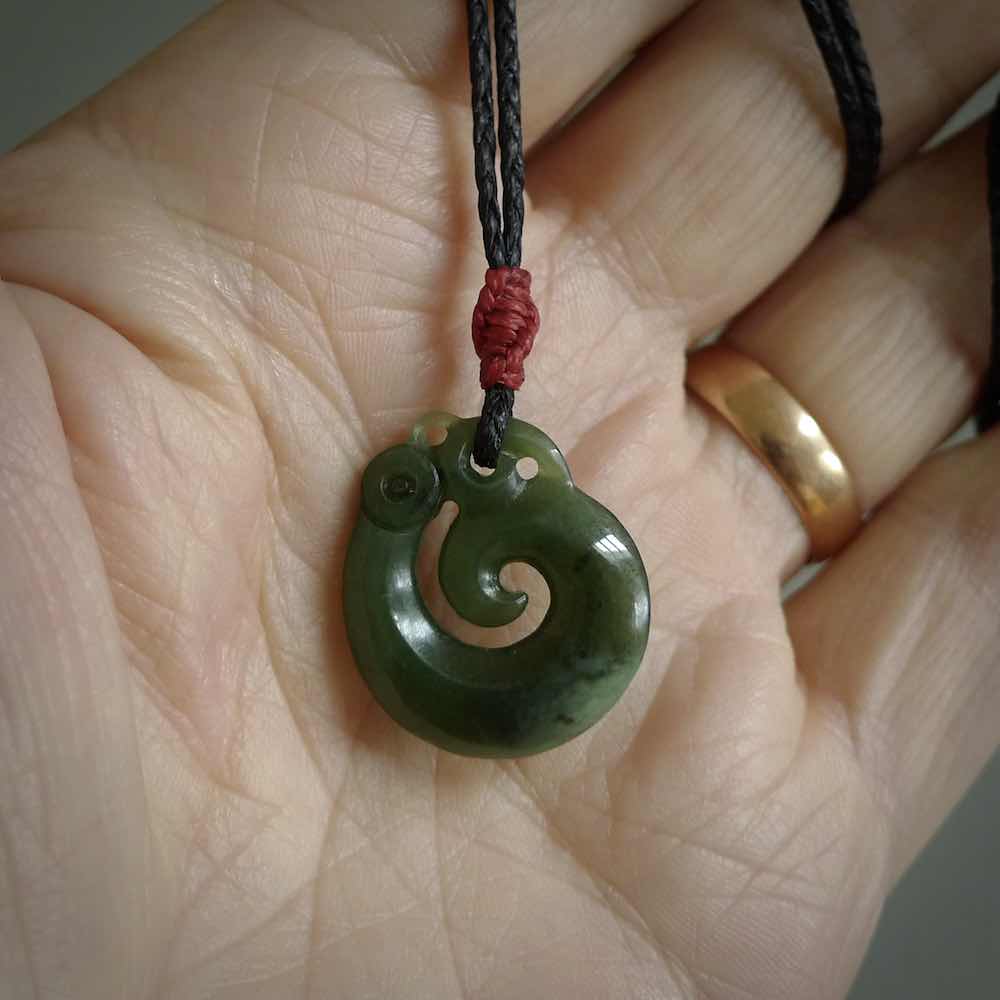 New Zealand Koru Manaia. Hand carved small jade koropepe pendant. Made in New Zealand. Real Jade, pounamu. Provided with an adjustable manuka green cord and packaged in a woven kete pouch.