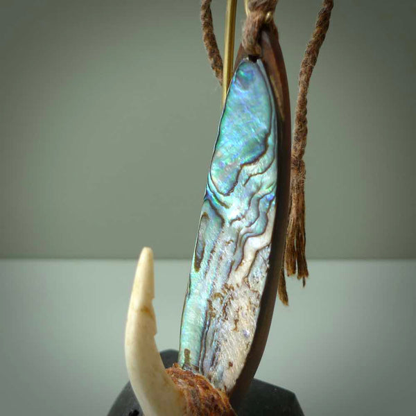 This picture shows a small sculptural hook called a pā kahawai. It is carved from whale bone, paua shell and wood, and is a colourful blue grey colour. It is shown on a stand made from argillite stone and is held in a brass cradle. One only, free shipping worldwide.