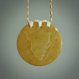 This piece is a large, oval round, disc pendant. It was carved for us by Alex Sands  from a lovely bright and orange piece of New Zealand Flower jade with incredible orange and greens colours at throughout the stone. It is suspended on a burnt gold and ice white coloured braided cord that is length adjustable.