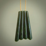 This picture shows a large jade contemporary pendant carved in a deep green coloured piece of marsden jade. This is a unique one off piece. It is suspended on a beige cord which is length adjustable.