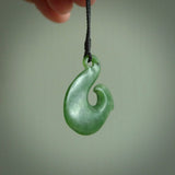 This picture shows a jade hook pendant, also called a hei-matau, carved for us in New Zealand jade. The jade is a wonderful pale mint green pounamu. This is a rare jade loved and valued for its distinctive colour. The carver is Ric Moor - and this is a beautiful example of his work. The cord is a four-plait, adjustable black coloured necklace.