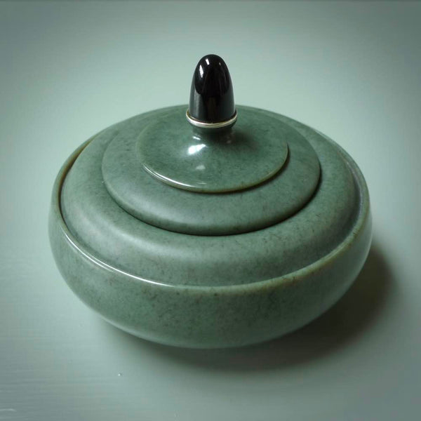 This photo shows a hand carved, Wyoming 'Sage' Nephrite Jade bowl sculpture. This 3.5 inch bowl carved from extremely fine-grained Sage. With Wyoming Black Jade and Sterling Silver, high domed centre grip. This hand crafted work of art was hand made by award winning New Zealand carver Donn Salt.