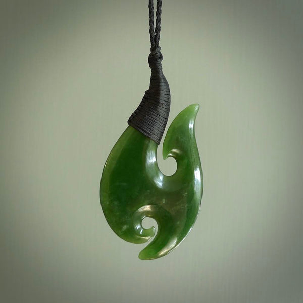 This is a beautiful New Zealand Pounamu, jade hook with a little decorative koru carved into the bottom. It is a chunky piece but beautifully balanced so doesn't look heavy. The cord is a Black colour and the binding on the top is also black.