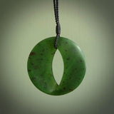 This photo shows a medium sized unique complex contemporary disc pendant. It is carved from a very light and semi translucent speckled piece of New Zealand kawakawa jade. It is finished in a soft matte that glows and is lovely to hold. We provide this with an adjustable cord in plain black. We ship this piece worldwide and shipping is included in the price.