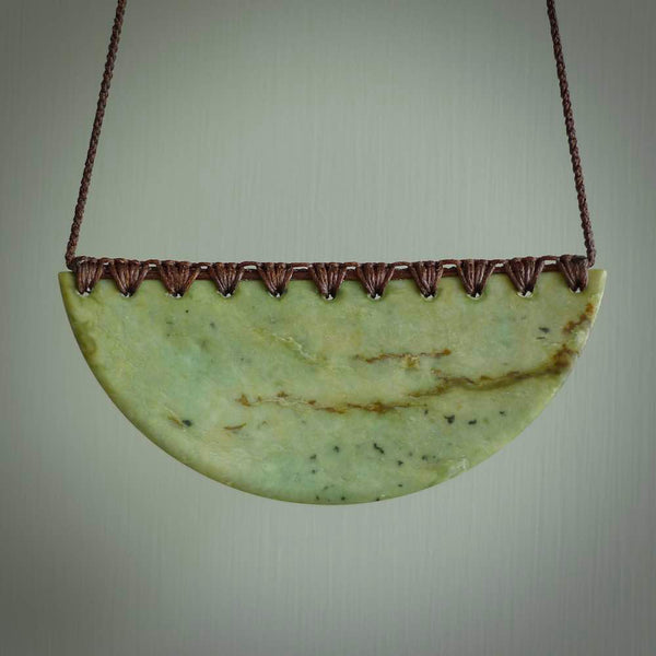 This picture shows a hand carved jade contemporary half-shield pendant. It is a light, minty green colour with orange shades and darker inclusions throughout. This is a wonderful piece of jewellery. The cord is hand plaited and adjustable so that you can position the pendant where it suits you best. This piece was carved for us by Ric Moor. Delivery is free worldwide.