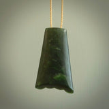 This picture shows a large jade contemporary pendant carved in a deep green coloured piece of marsden jade. This is a unique one off piece. It is suspended on a beige cord which is length adjustable.