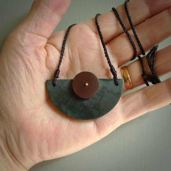 This piece is a contemporary shield pendant carved from New Zealand Jade. It is a deep green colour. The cord is black and is length adjustable. Hand made with Jade and Red Jasper Stone.