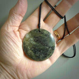 This piece is a large sized, oval round, disc pendant. It was carved for us by Raegan Bregman from a lovely green piece of New Zealand Inanga jade and Kokopu Jade. It is suspended on a Black coloured braided cord that is length adjustable.