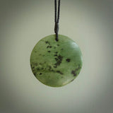 This piece is a large, oval round, disc pendant. It was carved for us by Ric Moor from a lovely deep and milky green piece of New Zealand kokopu jade. It is suspended on a black coloured braided cord that is length adjustable.