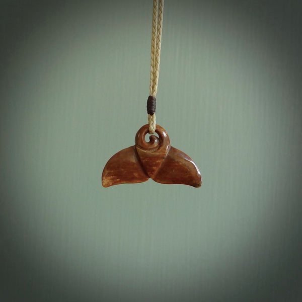 This photo shows a small whaletail pendant that we have carved from a dark honey coloured piece of Woolly Mammoth tusk. It is suspended on a Pale straw coloured cord that is length adjustable.