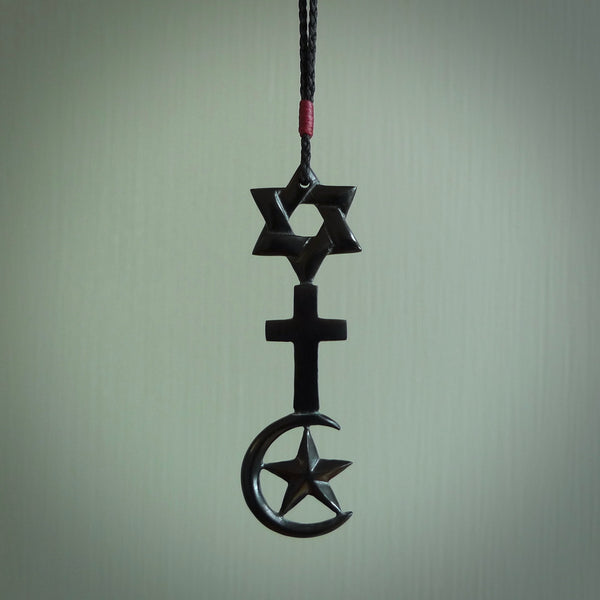This pendant is a series of religious symbols carved in one piece of black jade. The top is a star of david, next is a christian cross and at the bottom is the crescent of islam. It is suspended on a fine, plaited black cord which is length adjustable.