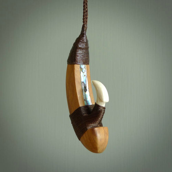 This picture shows a large matau, hook called a pā kahawai. It is carved from bone,  wood, and paua shell. One only, free shipping worldwide. Provided with an adjustable brown cord. Stunning work of Art to Wear by Andrew Doughty.