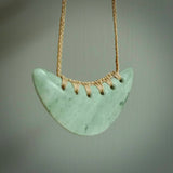 This picture shows a hand carved jade contemporary half-shield pendant. It is a light green and blue colour. This is a wonderful piece of jewellery. The cord is hand plaited and adjustable so that you can position the pendant where it suits you best. This piece was carved for us by Darren Hill. Delivery is free worldwide.