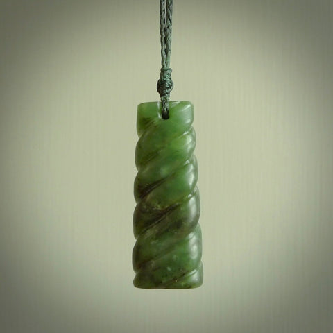 This piece is a toki pendant with a double twist through the body. It is carved from flower jade from New Zealand. It is a deep green colour. The cord is black and is length adjustable.