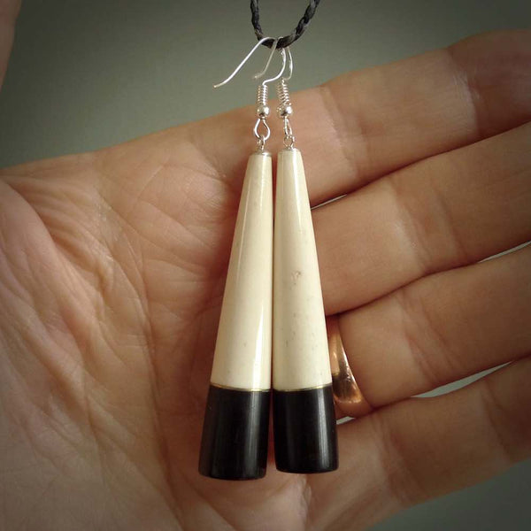 Hand carved earrings made from bone and buffalo horn. They are an elongated drop shape with a flat bottom. The bone is a nice creamy white and incorporates the top three quarters, and the bottom quarter is a beautiful black buffalo horn. These are wonderful handcrafted earrings.