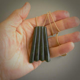 This picture shows a large jade contemporary pendant carved in a deep green coloured piece of marsden jade. This is a unique one off piece. It is suspended on a beige cord which is length adjustable.