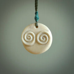 A hand carved and intricate koru pendant made for us by Yuri Terenyi. This is a beautiful little piece and is emblematic of the well known and loved Koru design. It is carved from bone in a round shape with decorative design carved into the koru. It is suspended from a sage cord with a paradise blue floret and the necklace is adjustable.