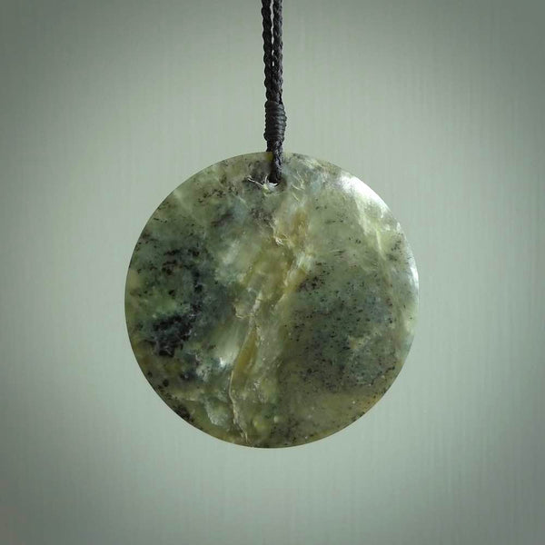 This piece is a large sized, oval round, disc pendant. It was carved for us by Raegan Bregman from a lovely green piece of New Zealand Inanga jade and Kokopu Jade. It is suspended on a Black coloured braided cord that is length adjustable.