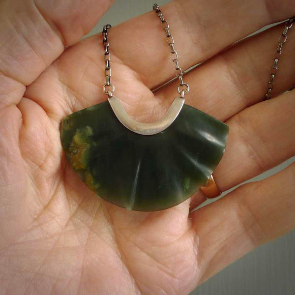This is a very dark green fan design pendant that we has been carved here in New Zealand by Josey Coyle. It is carved from a piece of New Zealand Marsden flower Jade pounamu with Sterling Silver fittings and a sterling silver chain. A contemporary fan shaped pendant made to wear.