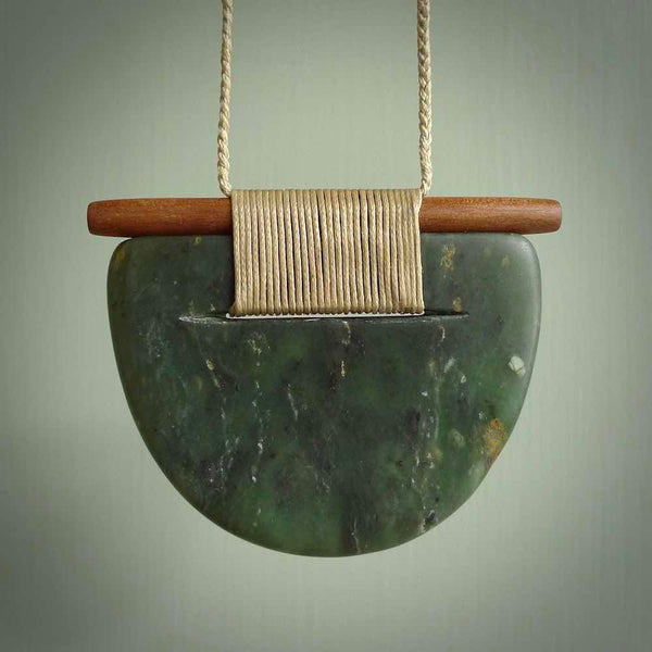 Raukaraka Pounamu breastplate pendant with rata wood. Hand carved by Rhys Hall for NZ Pacific. Handmade jewellery for sale online. The cord is a 3-braid plait in beige and has a loop and pebble toggle closure. Breastplate necklace for men and women. Scandinesian breastplate necklace hand made from New Zealand Jade.