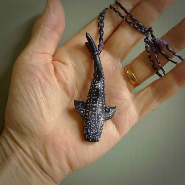 This picture shows a hand carved bone whale shark. It is stained with a special tea dye and is a very detailed piece. It has a hand plaited cord that is length adjustable so that it can be worn as a pendant.