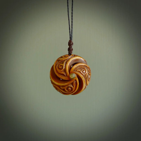 A hand carved and intricate koru pendant made for us by Yuri Terenyi. This is a beautiful little piece and is emblematic of the well known and loved Koru design. It is carved from bone in a hollowed, oval ball shape with decorative design carved into the koru. It is suspended from a Black cord with a wapiti brown floret and the necklace is adjustable.