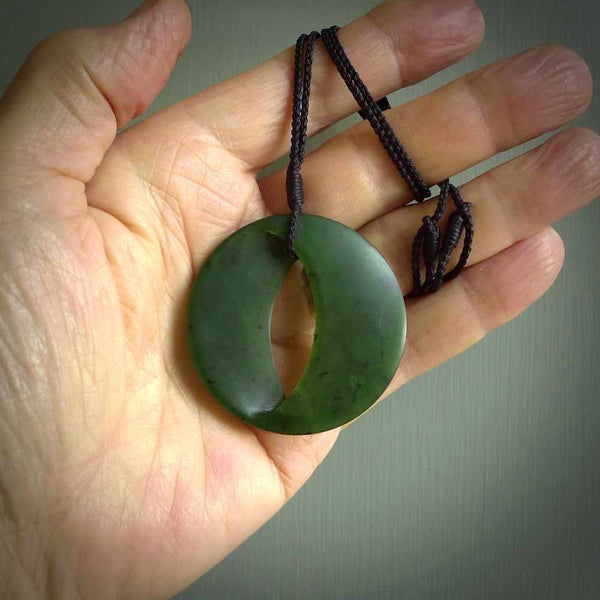 This photo shows a medium sized unique complex contemporary disc pendant. It is carved from a very light and semi translucent speckled piece of New Zealand kawakawa jade. It is finished in a soft matte that glows and is lovely to hold. We provide this with an adjustable cord in plain black. We ship this piece worldwide and shipping is included in the price.