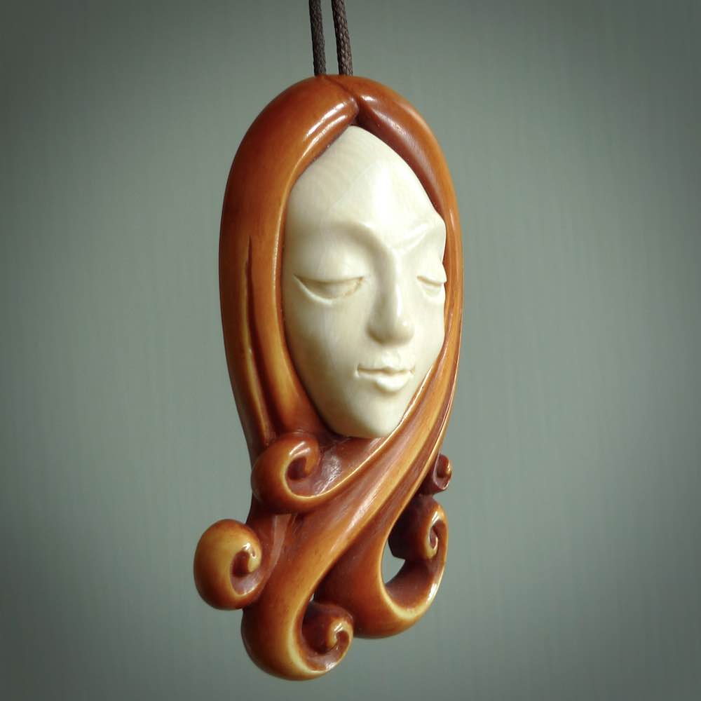 This is a hand carved bone contemporary female pendant. Yuri Terenyi has carved this from Stained Bone with Woolly Mammoth Tusk and Paua Shell inlay on the back of the pendant. It is a delightful, large and artistic piece of jewellery. One only necklace. The necklace is provided on an adjustable cord in a hand made, custom, wooden box.