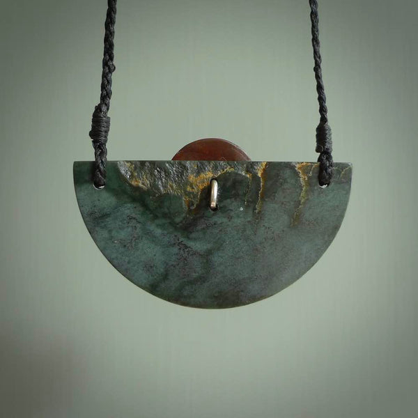 This piece is a contemporary shield pendant carved from New Zealand Jade. It is a deep green colour. The cord is black and is length adjustable. Hand made with Jade and Red Jasper Stone.