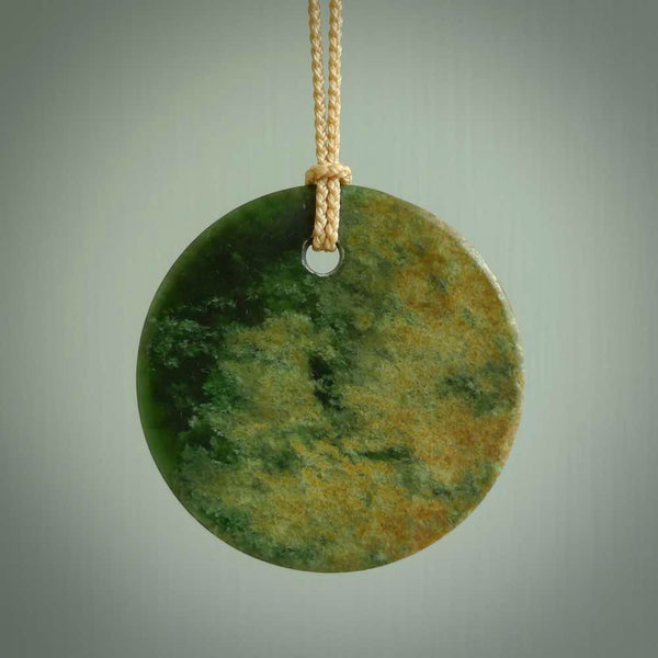 This piece is a large oval round, disc pendant. It was carved for us by Ric Moor from a lovely orange and green piece of New Zealand flower jade. It is suspended on a beige coloured braided cord that is length adjustable.