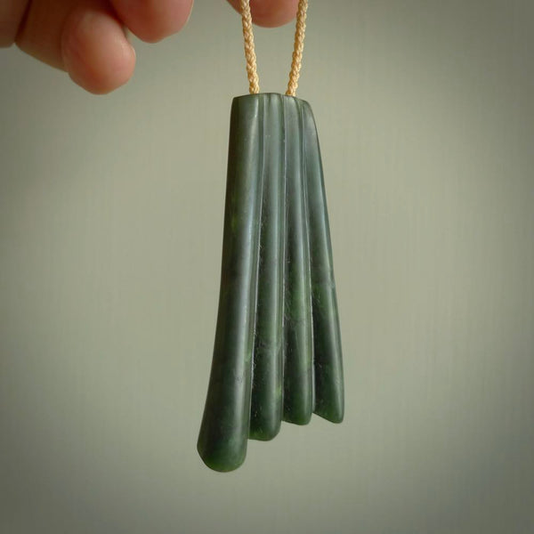 This picture shows a large jade contemporary pendant carved in a deep green coloured piece of marsden jade. This is a unique one off piece. It is suspended on a beige cord which is length adjustable.