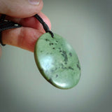 This piece is a large, oval round, disc pendant. It was carved for us by Ric Moor from a lovely deep and milky green piece of New Zealand kokopu jade. It is suspended on a black coloured braided cord that is length adjustable.