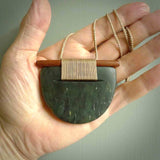 Raukaraka Pounamu breastplate pendant with rata wood. Hand carved by Rhys Hall for NZ Pacific. Handmade jewellery for sale online. The cord is a 3-braid plait in beige and has a loop and pebble toggle closure. Breastplate necklace for men and women. Scandinesian breastplate necklace hand made from New Zealand Jade.