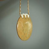This piece is a large, oval round, disc pendant. It was carved for us by Alex Sands  from a lovely bright and orange piece of New Zealand Flower jade with incredible orange and greens colours at throughout the stone. It is suspended on a burnt gold and ice white coloured braided cord that is length adjustable.