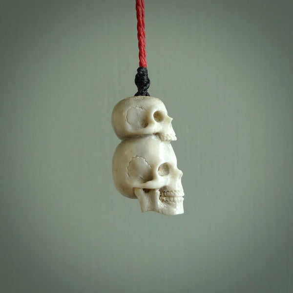 This photo shows a double skull pendant hand carved in deer antler. It is provided with a plaited cord necklace which is length adjustable.