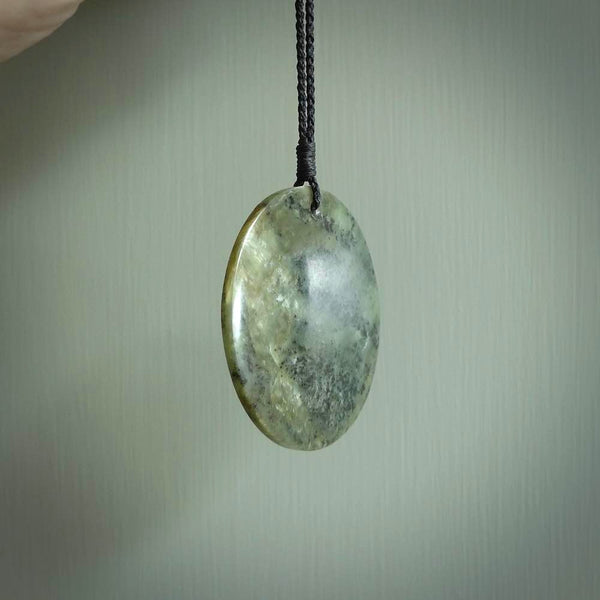 This piece is a large sized, oval round, disc pendant. It was carved for us by Raegan Bregman from a lovely green piece of New Zealand Inanga jade and Kokopu Jade. It is suspended on a Black coloured braided cord that is length adjustable.